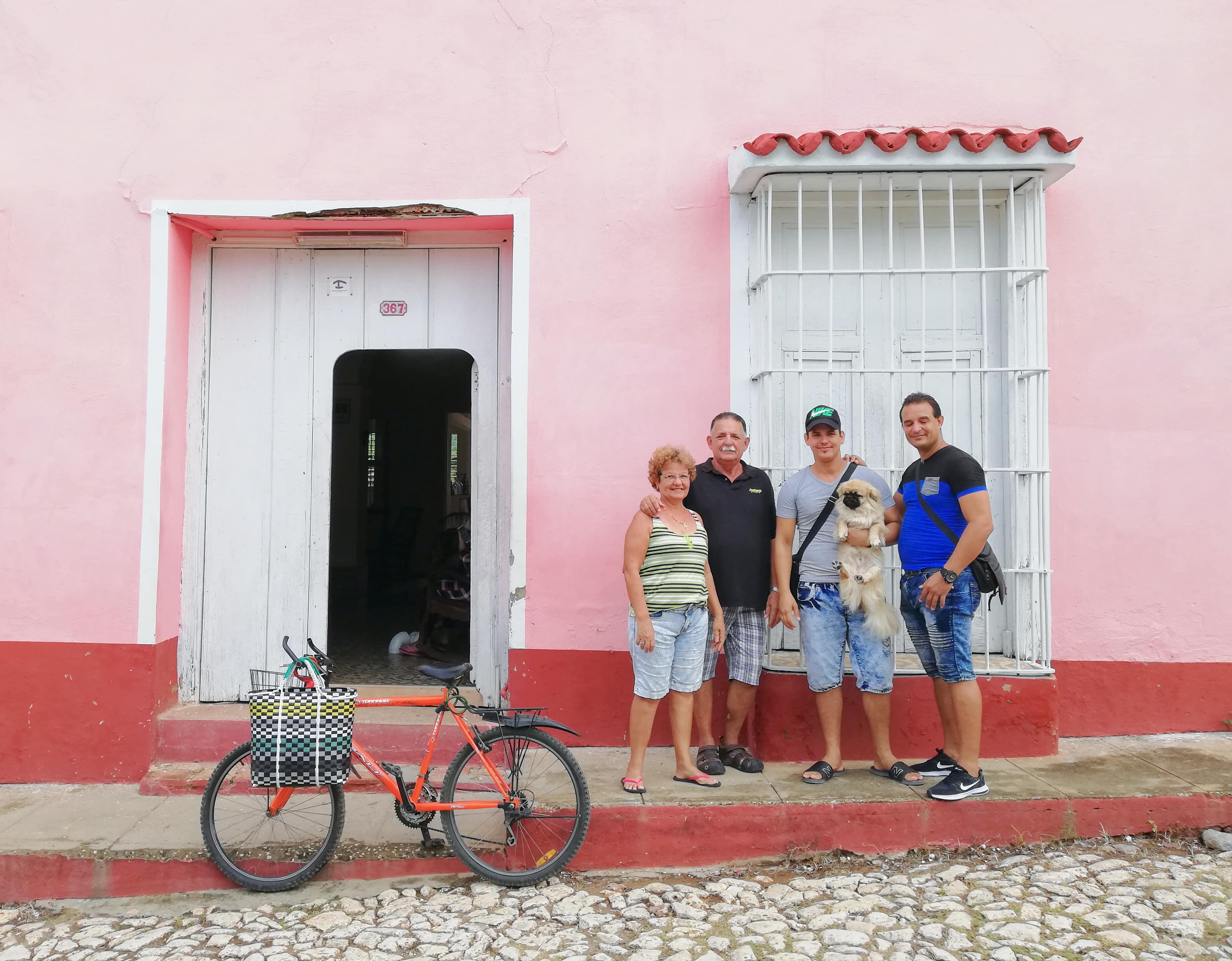 Uma famila frente à sua guesthouse em Trinidad, Cuba Família cubana sorri em frente à sua guesthouse, com fachada rosa e clima acolhedor