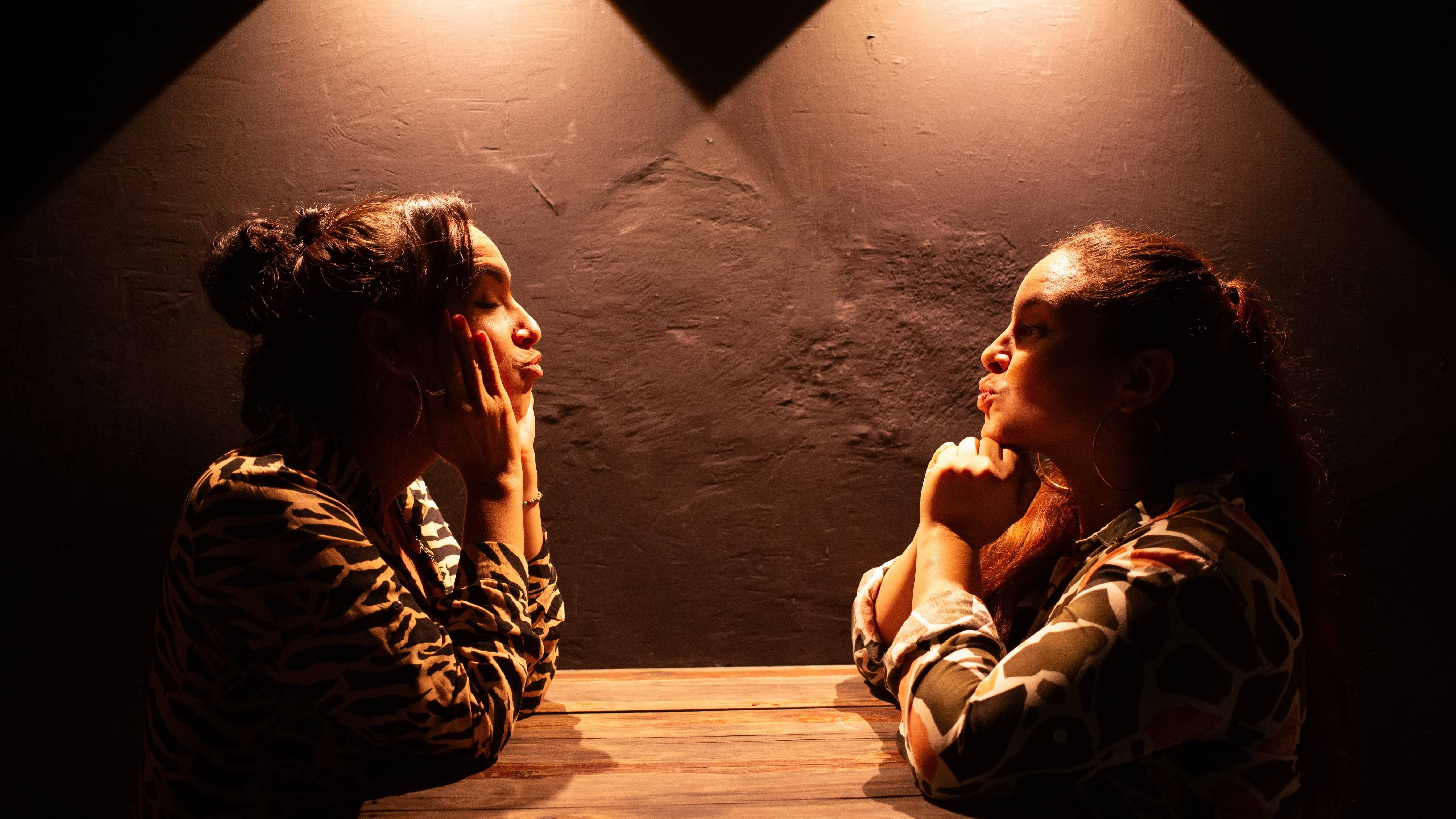 A female couple faces each other at a table, making kissy faces A female couple faces each other at a table, making kissy faces