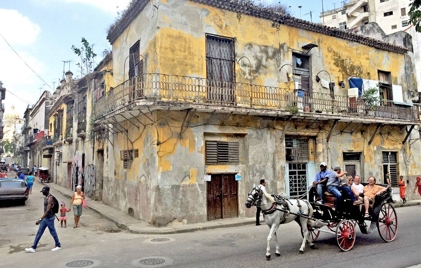 A horse and carriage driving past an old building in Havana A horse and carriage driving past an old building in Havana