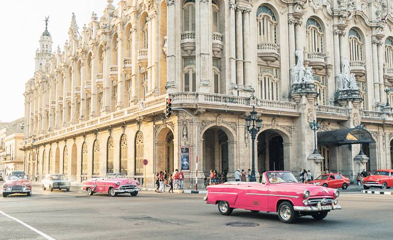A pink classic American car driving past the Gran Theatre in Havana A pink classic American car driving past the Gran Theatre in Havana