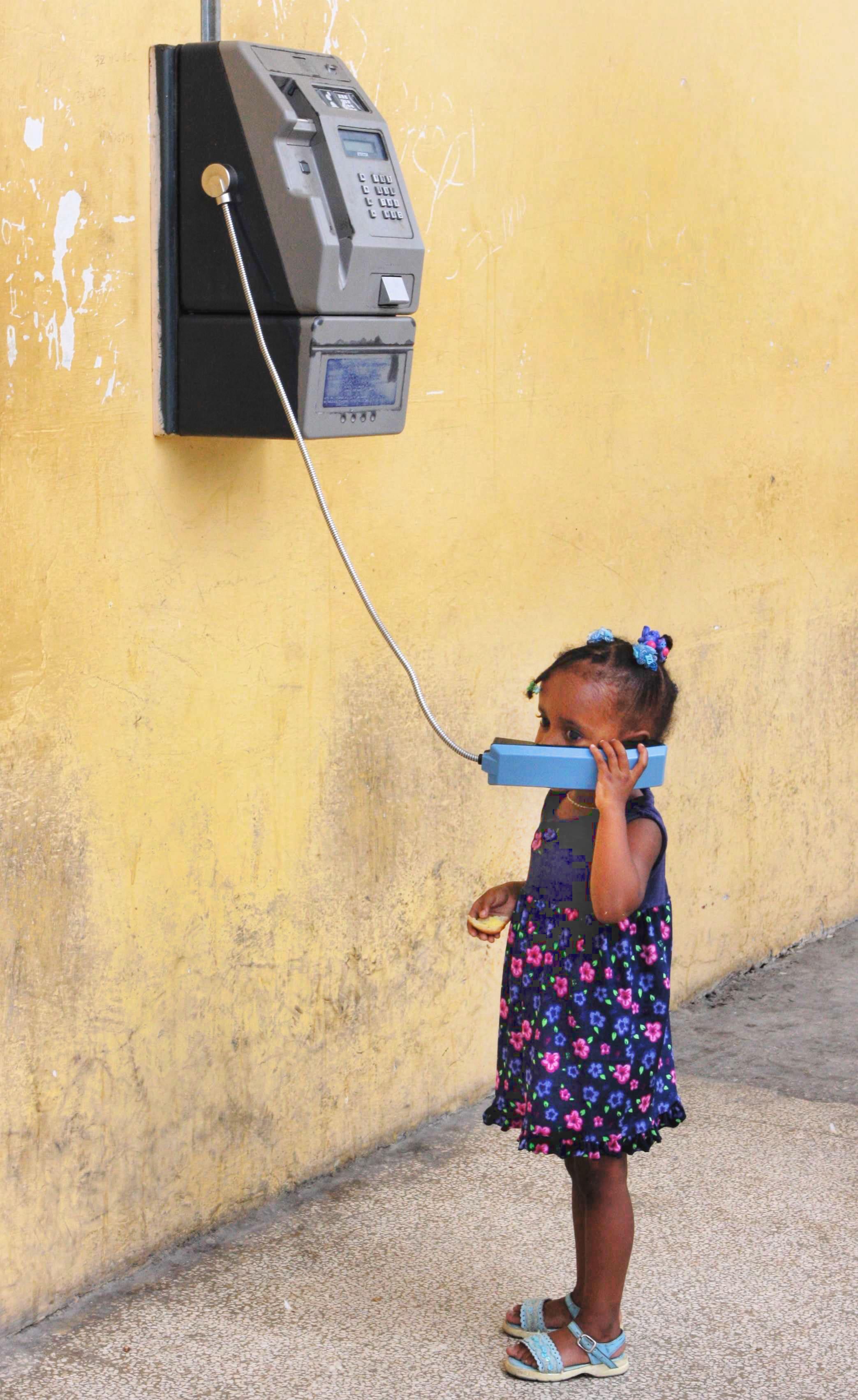 Uma menina pequena usando orelhão público em Cuba