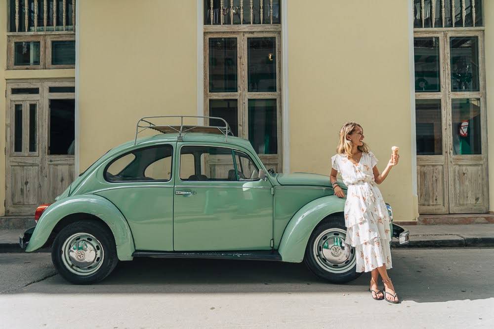 A woman holds an ice cream and leans on a green VW bug A woman holds an ice cream and leans on a green VW bug