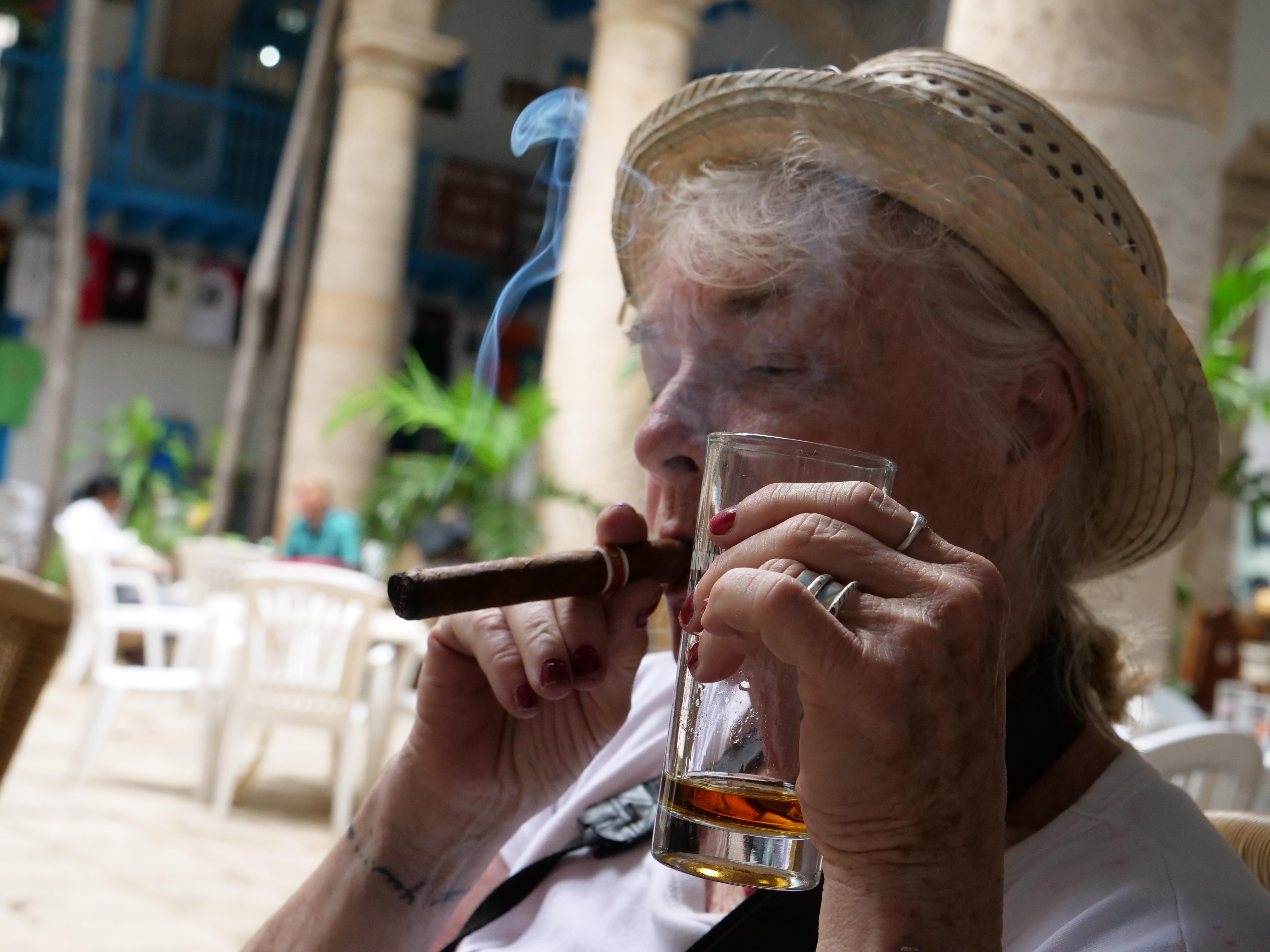 A woman in a straw hat enjoys smoking a Cuban cigar with a glass of rum