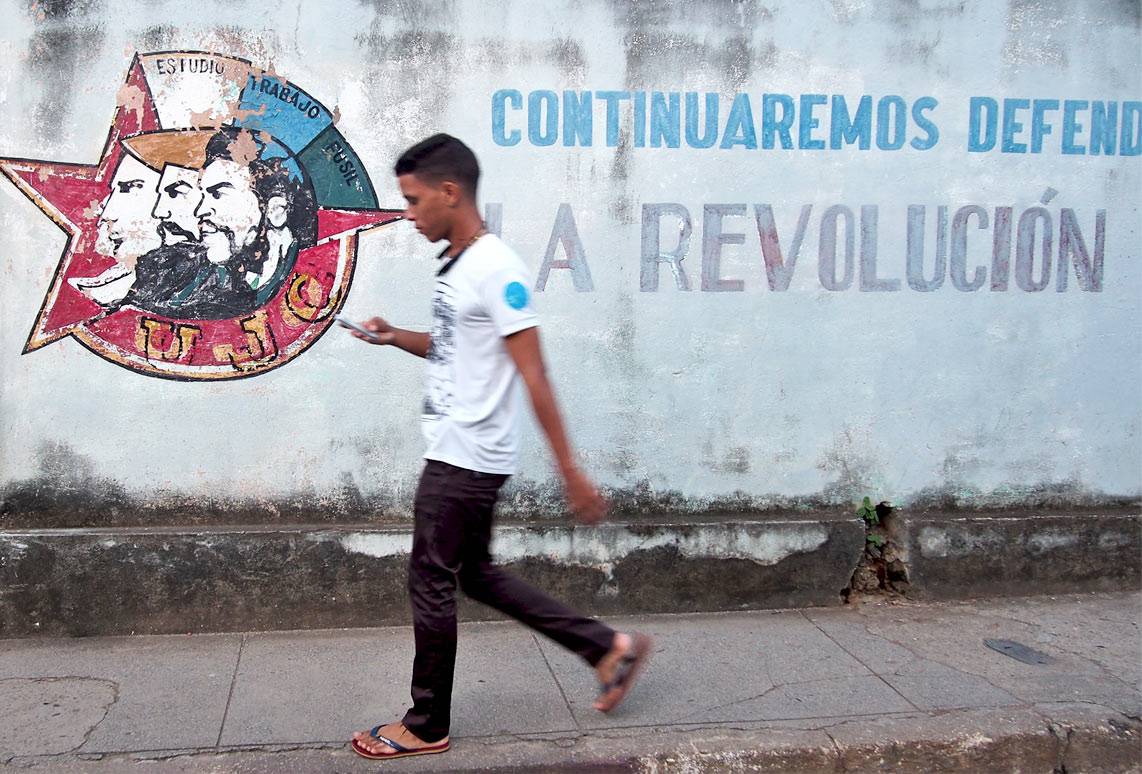 A young Cuban walking along the street using his mobile phone A young Cuban walking along the street using his mobile phone