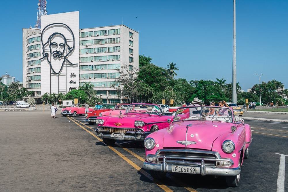 Camilo Ciefuegos decorates the telecommunications building in Plaza de la Revolucion, Old Havana Pink convertibles parked in front of building decorated with iron outline of Camilo Cienfuegos’ face