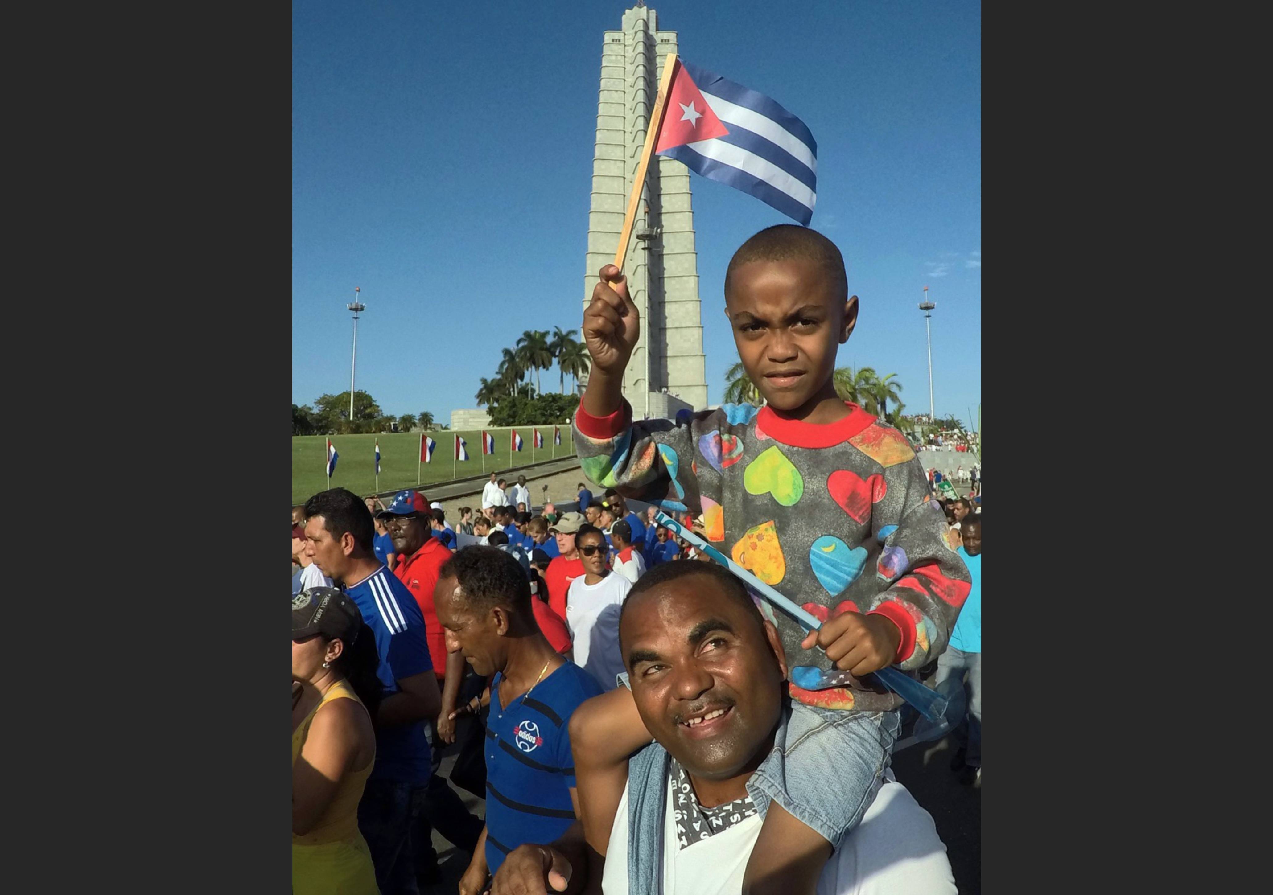 More flag waving and shoulder riding at the May Day Parade A young Cuban atop his fathers shoulders waves a Cuban flag at the May Day Parade in Havana