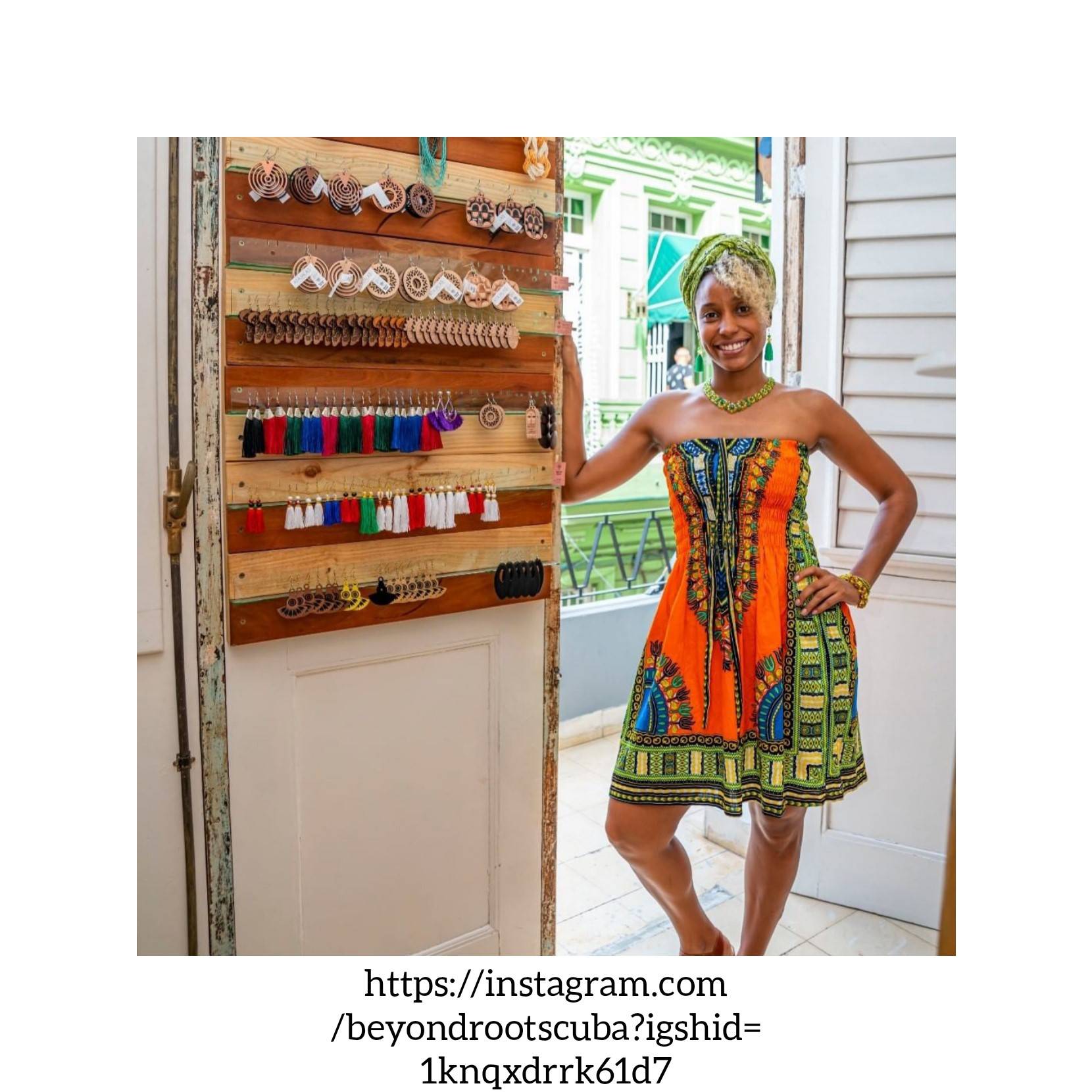 Photo Credit: Beyond Roots woman in colorful African style print dress stands next to wall display of earrings