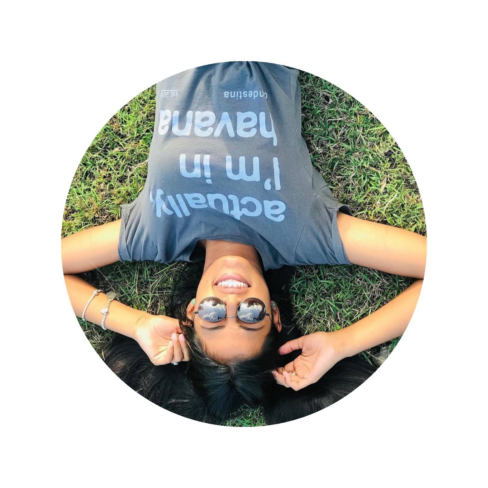 Photo Credit: Clandestina a young smiling woman in sunglasses and a Clandestina t-shirt lays in the grass