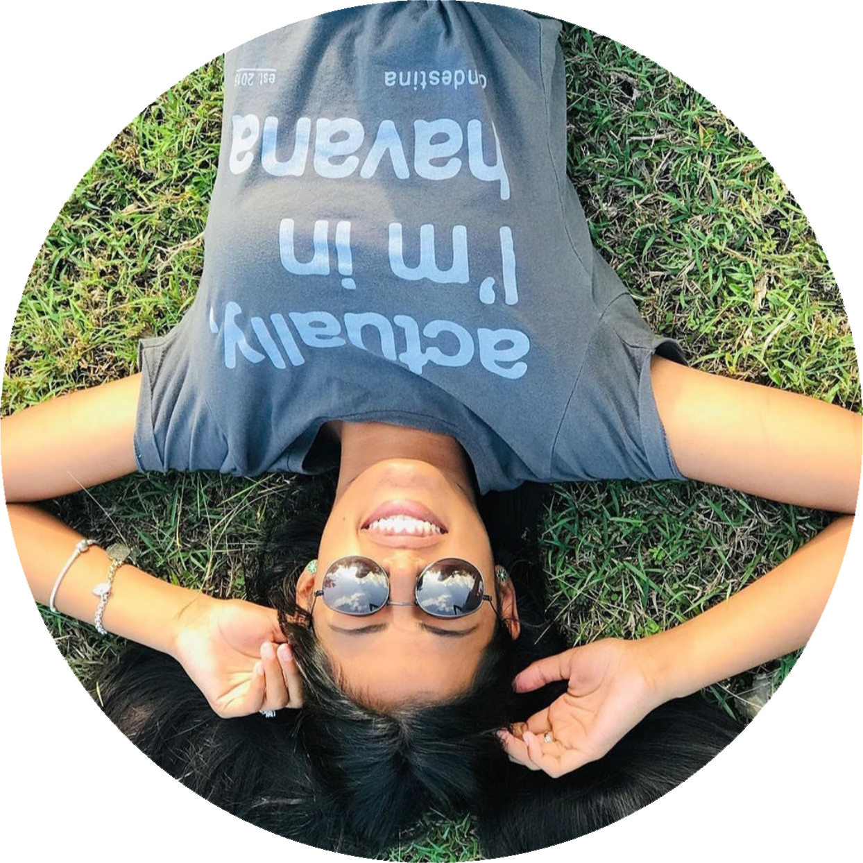 Photo Credit: Clandestina a young smiling woman in sunglasses and a Clandestina t-shirt lays in the grass