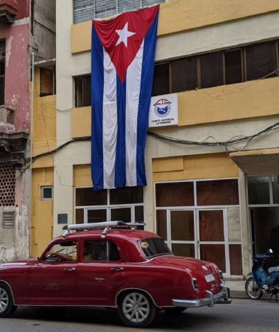 Red classic car in front of building adorned with Cuban flag