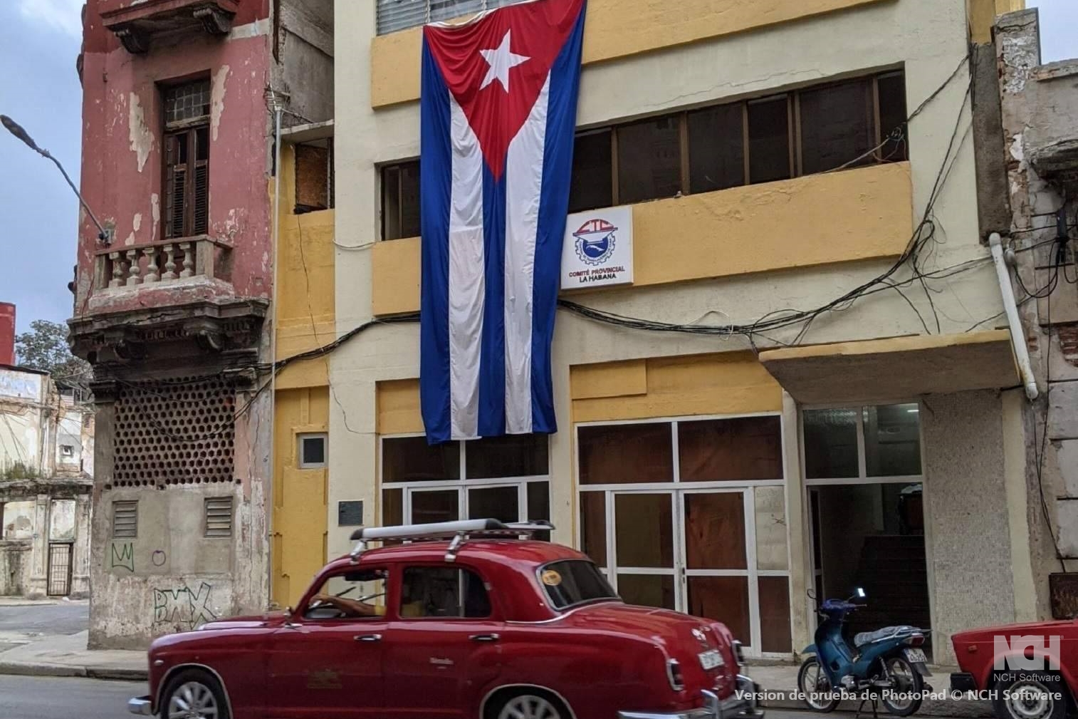 Red classic car in front of building adorned with Cuban flag