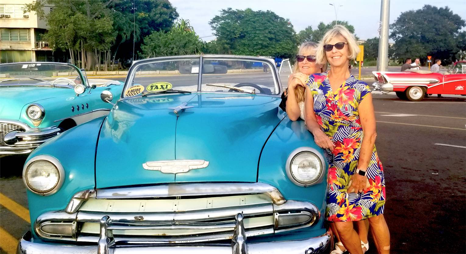 Two women lean against a blue convertible in Havana